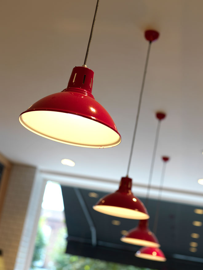 The bakery counter is lit by a row of red lamps Red pendant lamps light the bakery counter area
